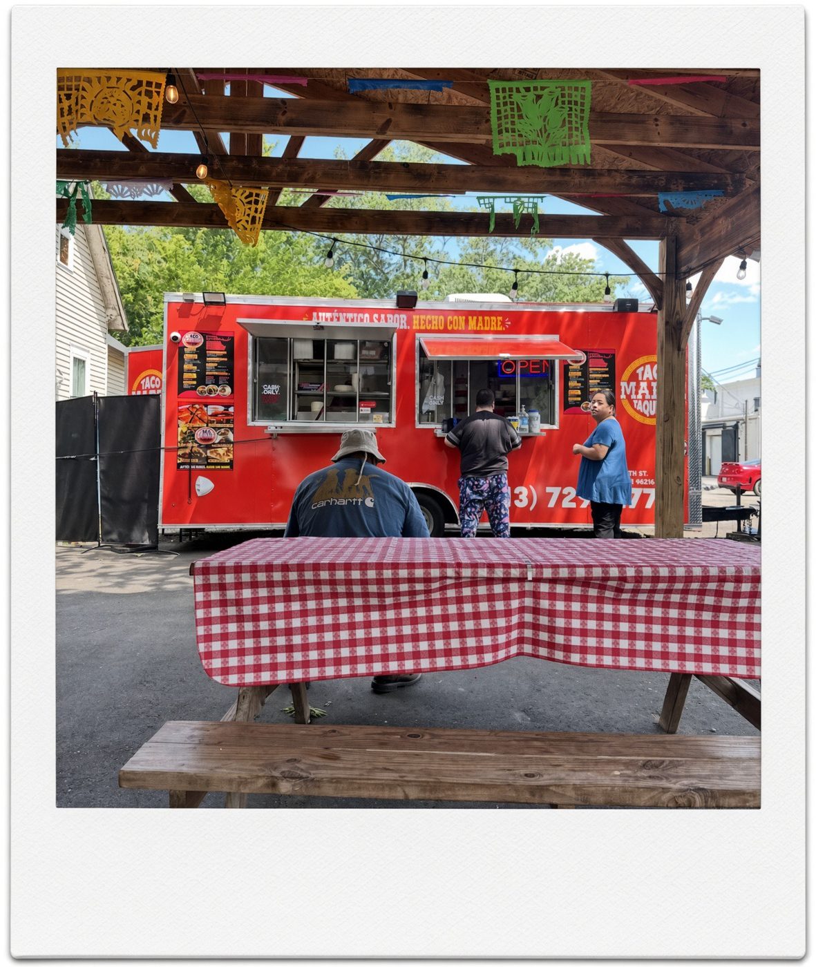 The red Taco Madre Taqueria food truck with picnic tables under a covered patio in Southwest Detroit
